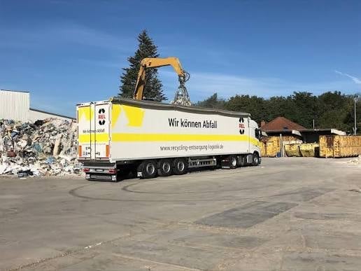 Yellow and white waste management truck with crane loading recycled materials at industrial facility
